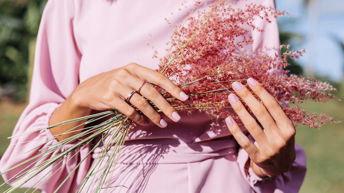Woman in a soft pink dress holding pink wildflowers, showing off glossy pastel pink Bio Sculpture gel nails perfect for spring and summer in Taunton.