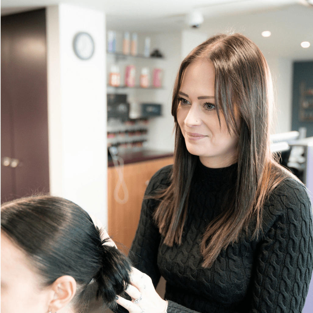 Jordan, a professional stylist at Honeys Hair & Beauty in Taunton, focuses carefully while styling a client’s hair. With sleek brunette hair and a calm expression, she reflects the salon’s expert, caring approach.