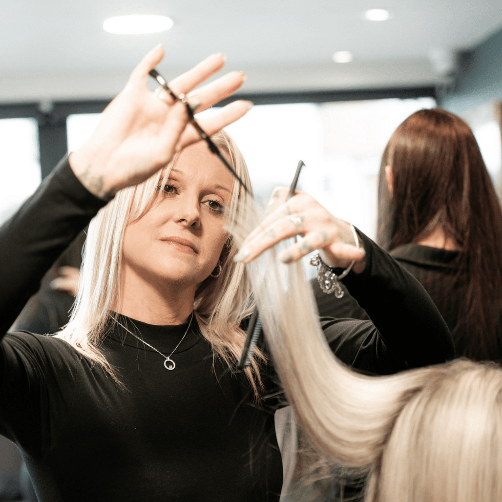 Zoe, a stylist at Honeys Hair & Beauty in Taunton, is captured mid-haircut with intense focus. Her platinum blonde hair and sleek black outfit convey both skill and style as she delivers precision results.